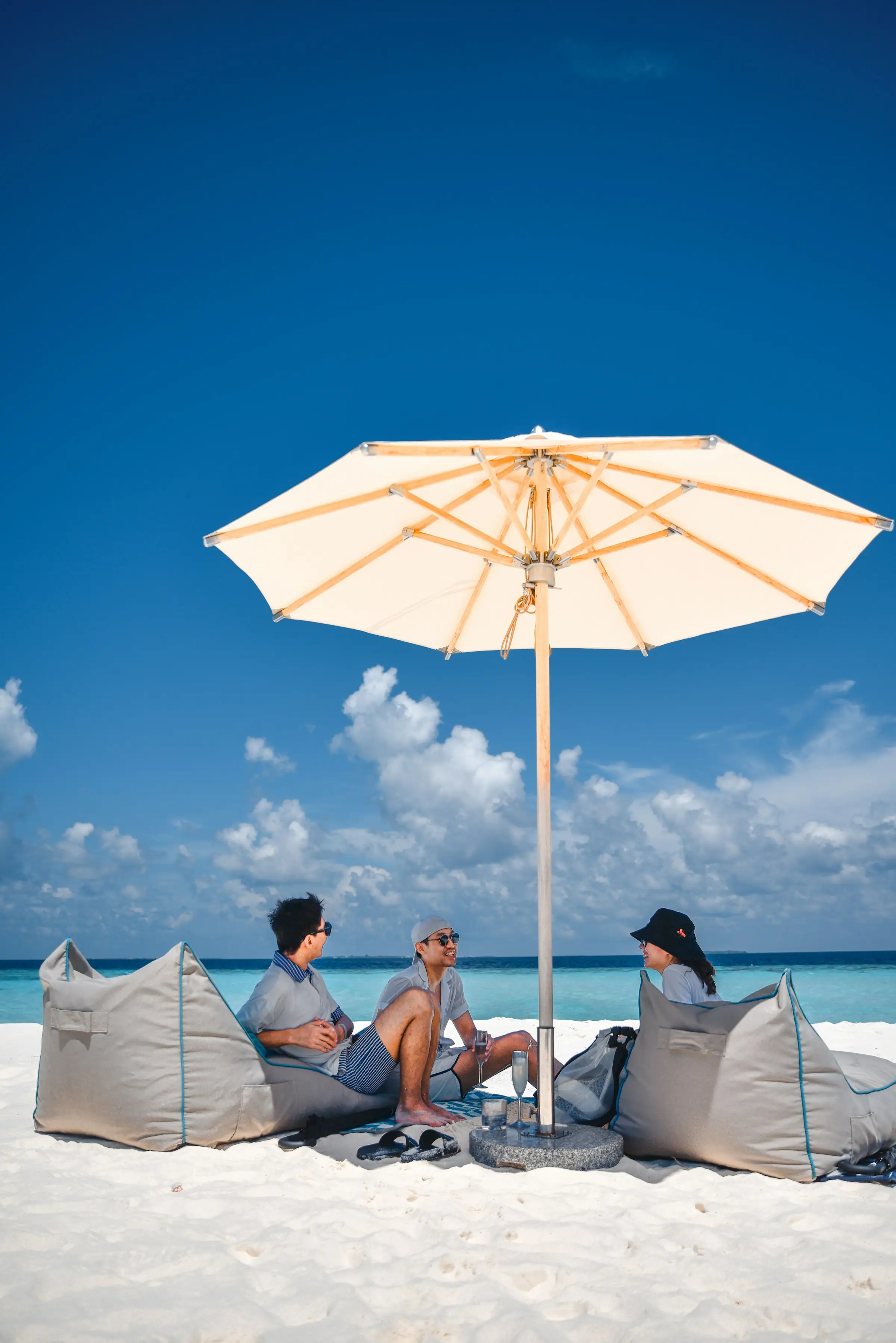 Three guests relaxing on bean bags under a parasol on a white sand beach