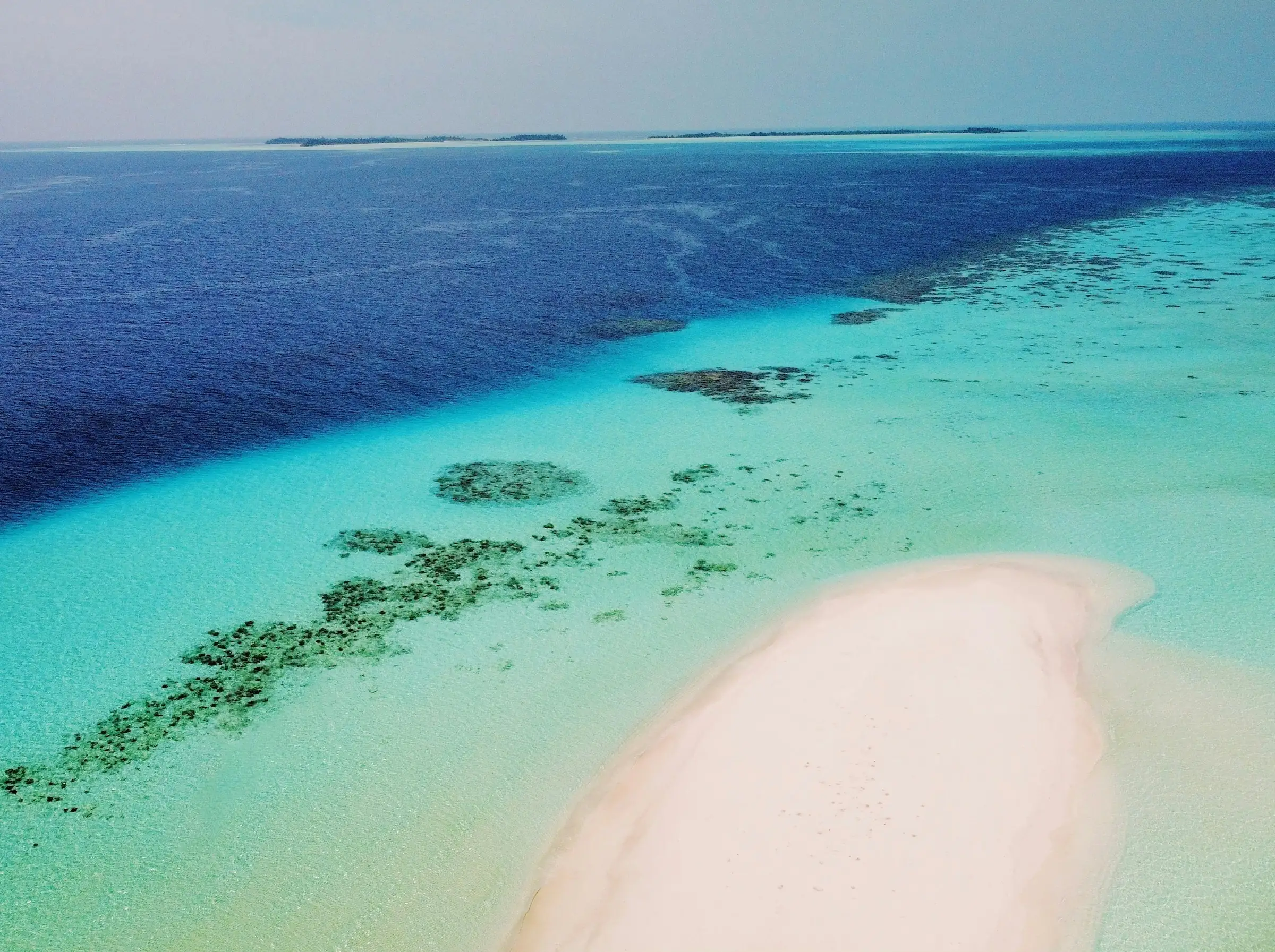 Aerial view of a white sandbank beside a reef in clear turquoise water