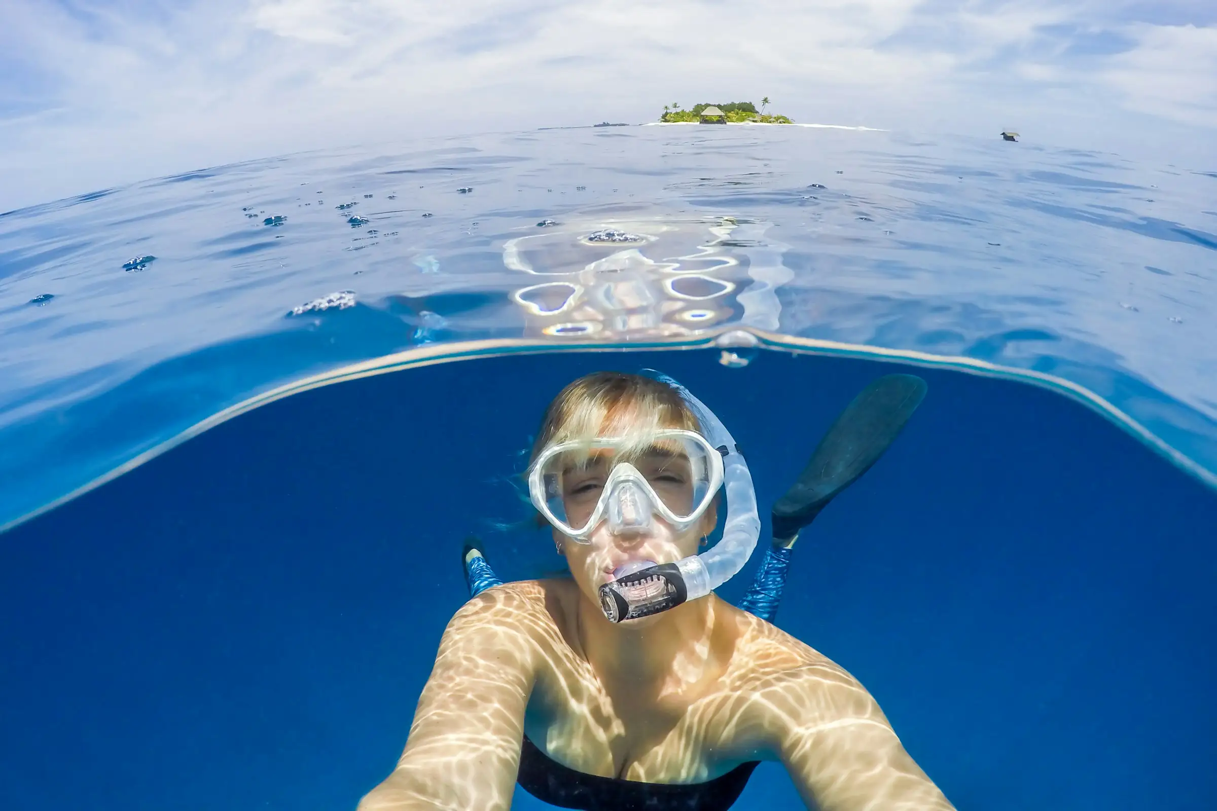 A snorkeller smiling at the camera just below the surface, with an island on the horizon