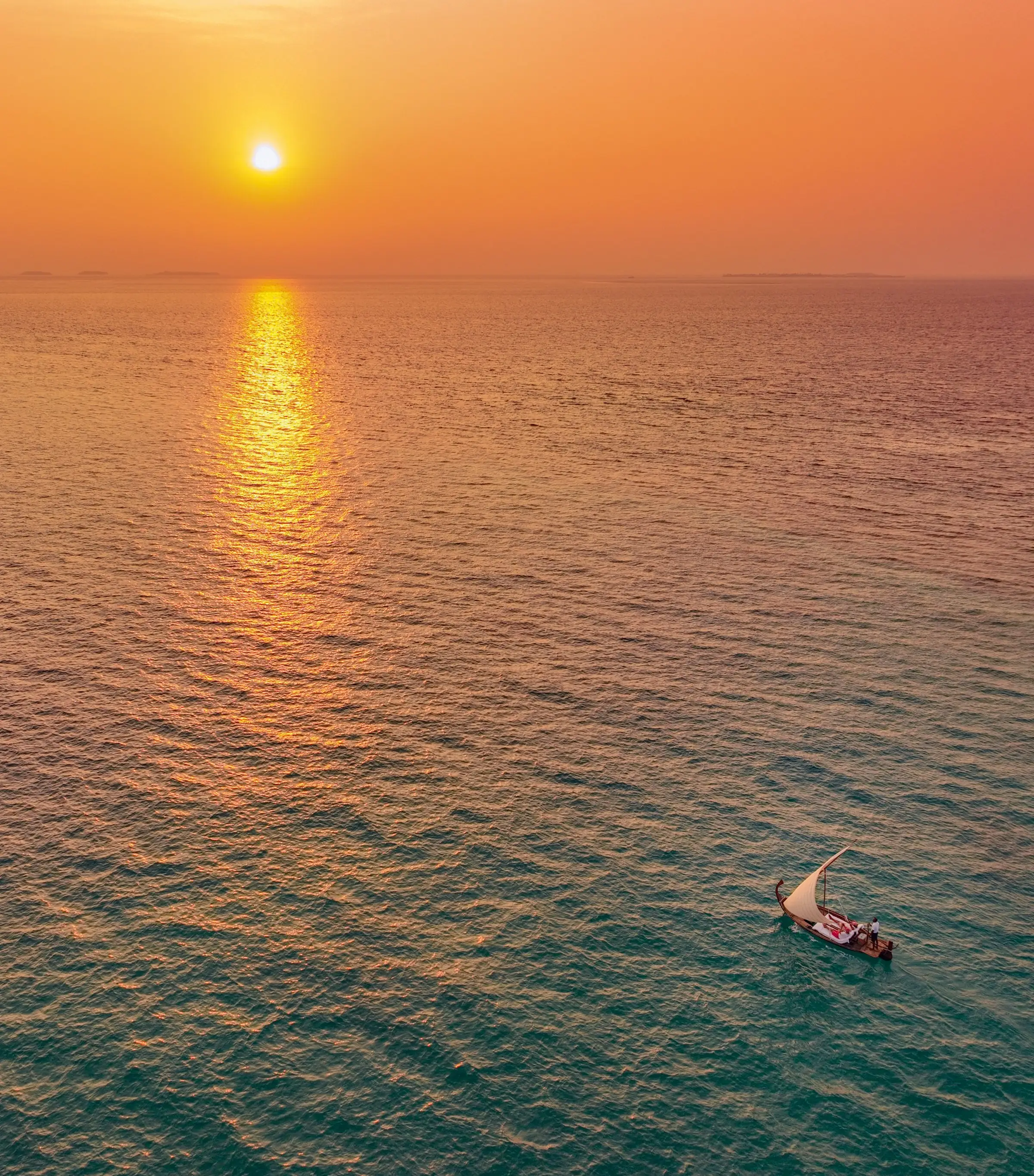 A dhoni crossing a calm lagoon at sunset, the sun low over the water