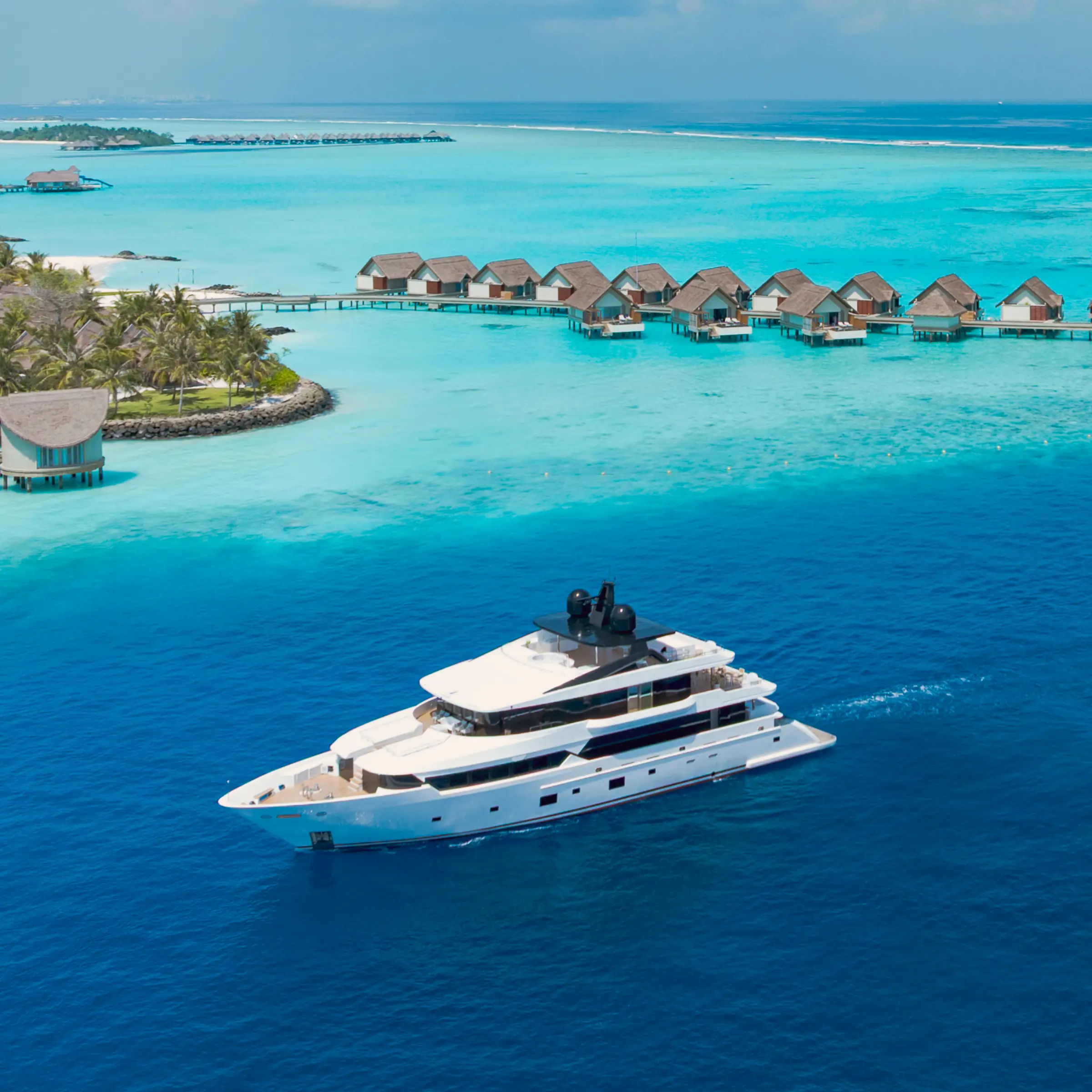 A white yacht cruising past an island with overwater villas